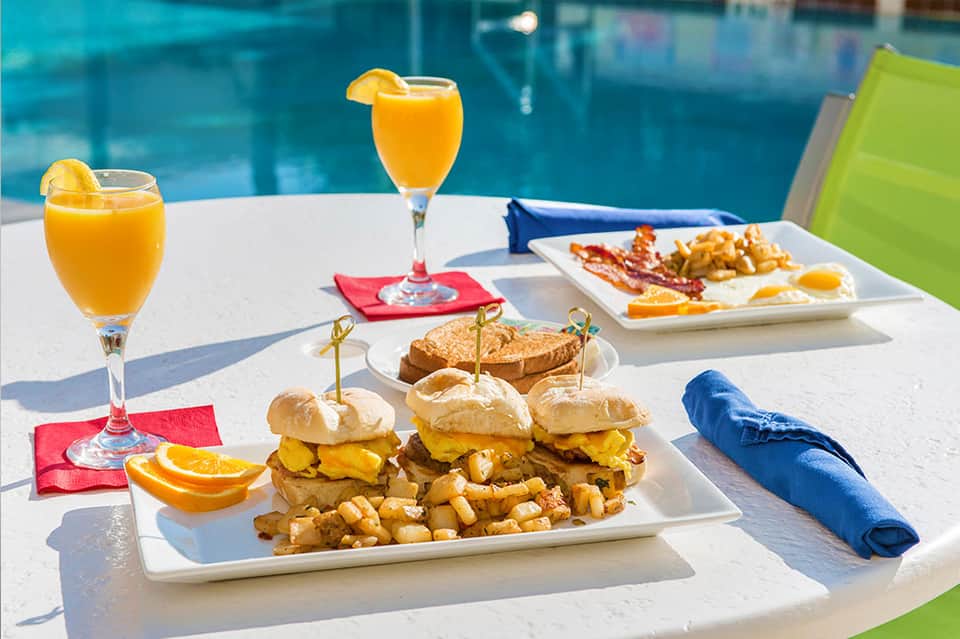 Poolside breakfast spread with burgers, fries, orange juice, and citrus slices