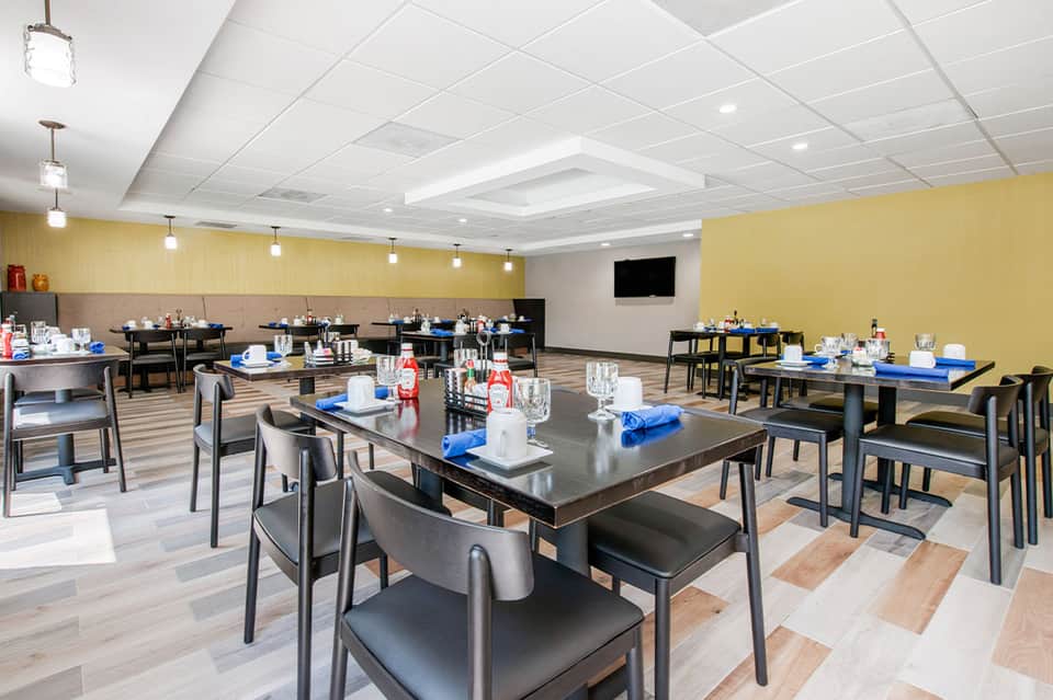 Modern dining room with yellow walls, black tables, blue napkins, and contemporary pendant lighting