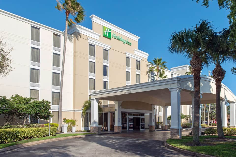 Holiday Inn hotel entrance with covered portico, palm trees, and manicured landscaping