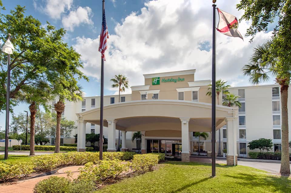 Holiday Inn hotel exterior with palm trees, covered entrance, and American flag on grounds