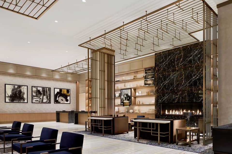 Luxury modern hotel lobby with fireplace, gold metal screens, shelving, and blue seating
