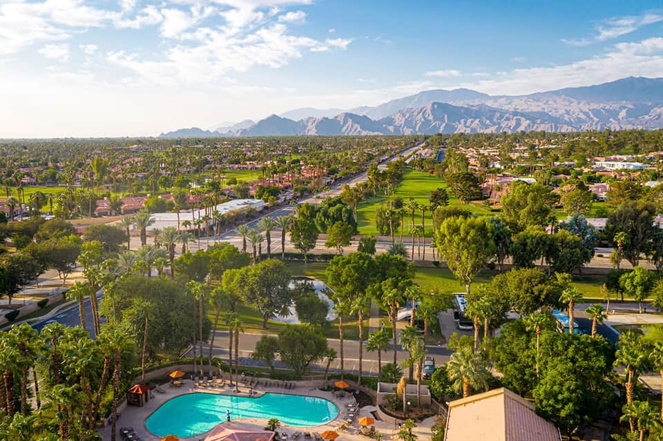 Aerial view of desert resort with pool, palm trees, and mountains in background