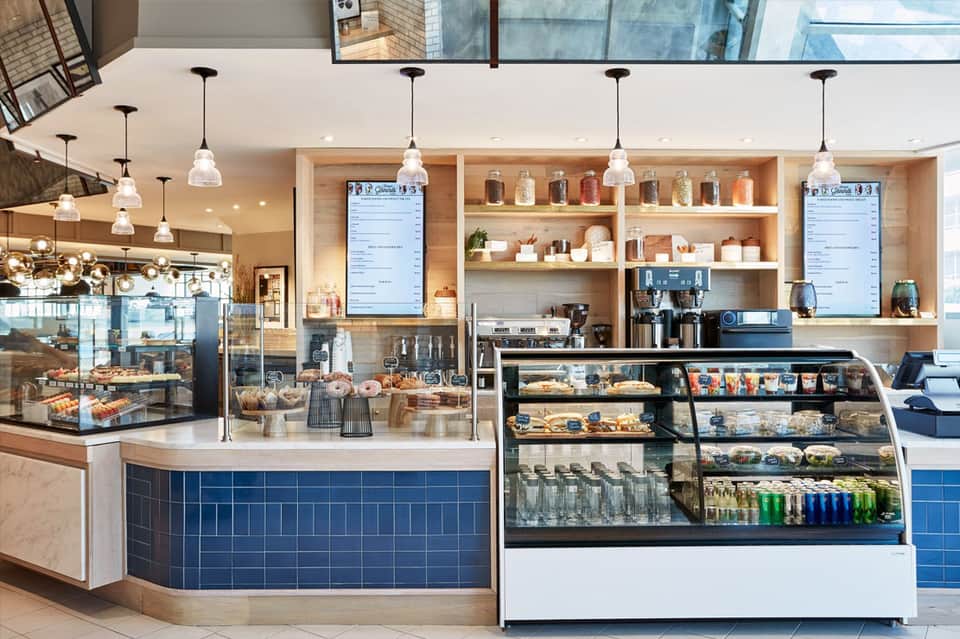Modern café interior with blue tile accents, wooden shelving, pendant lighting, and pastry display cases