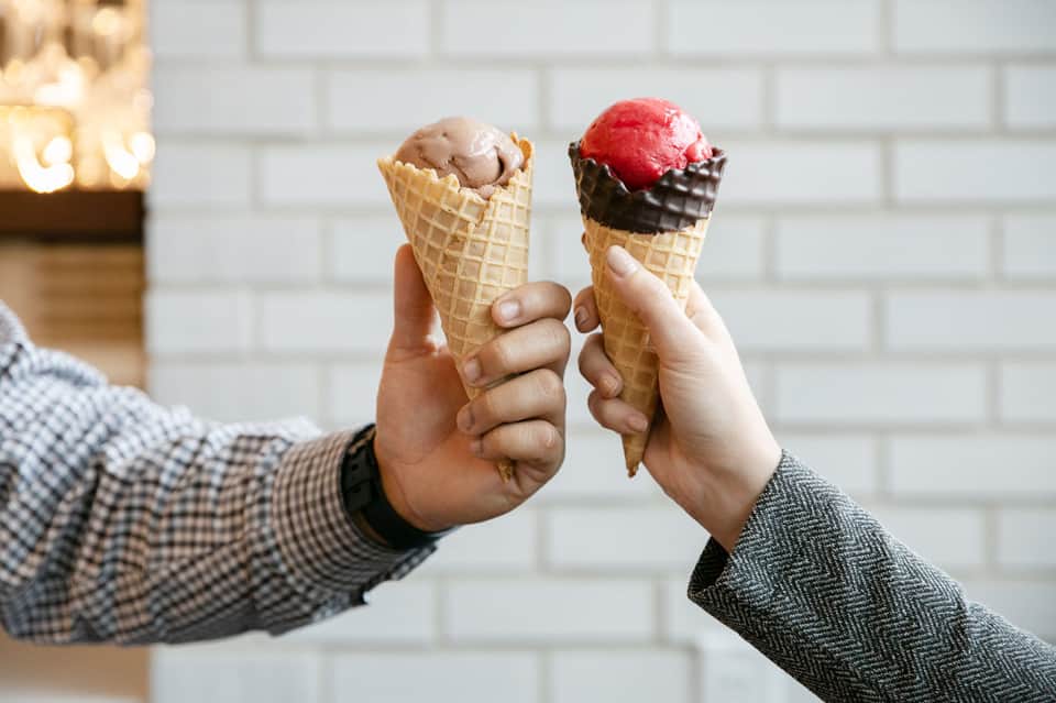 Two ice cream cones held up, one chocolate and one strawberry with chocolate dip