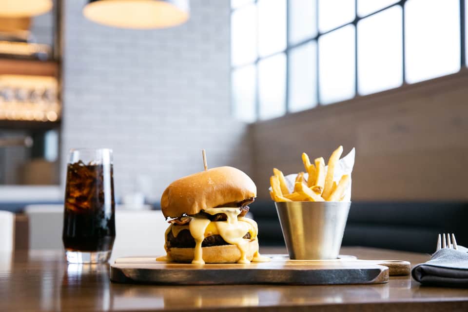 Gourmet burger with melted cheese and golden fries on slate board, modern dining