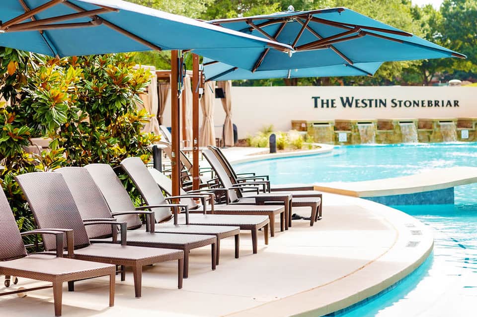 Resort poolside lounge chairs with blue umbrellas and landscaping at The Westin Stonebriar