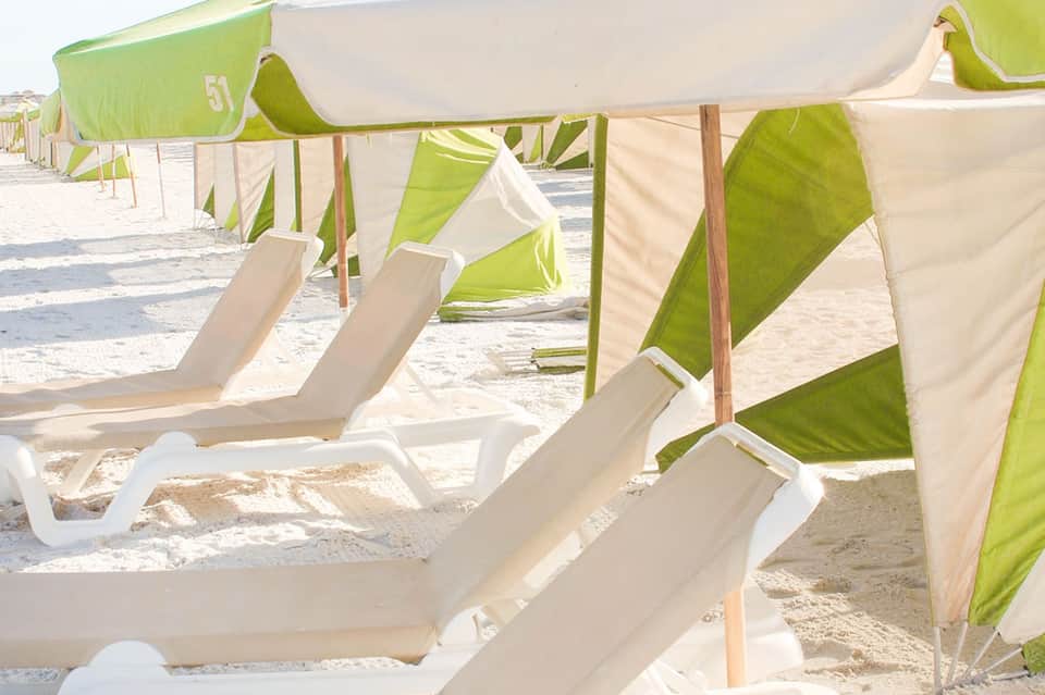 Beach cabanas with green and white striped canopies and lounge chairs on sandy shore