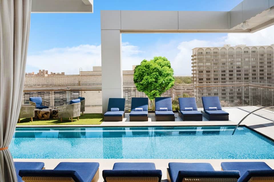 Rooftop pool deck with blue loungers, modern pergola, city skyline, and lounge seating