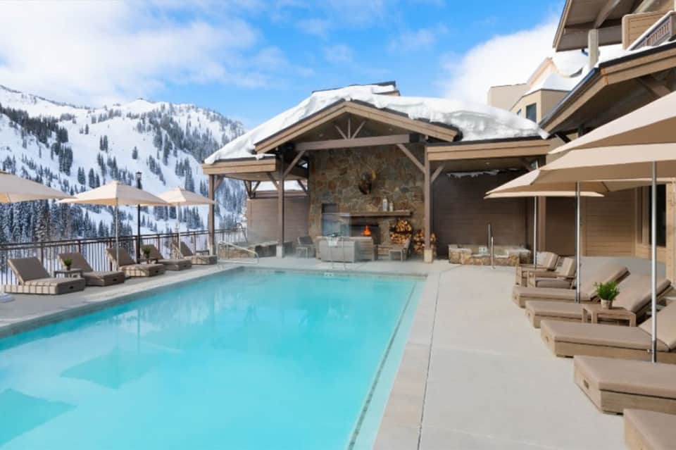 Luxury resort pool with mountain views, fire pit, and lounge seating in snow