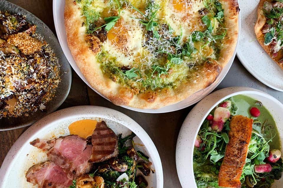 Gourmet pizzas and meat dishes plated on white bowls at restaurant