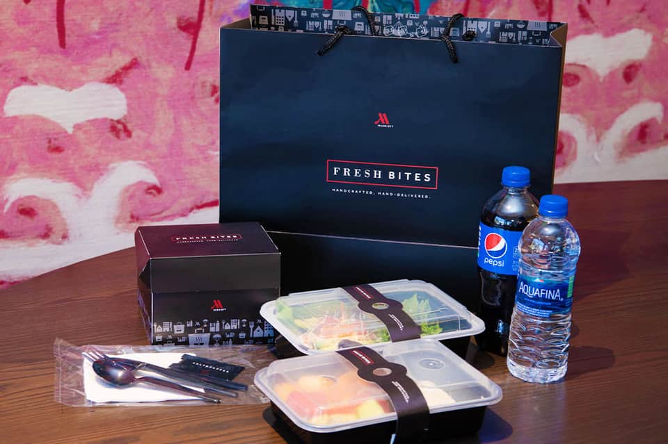 Fresh Bites catering delivery with prepared meals, beverages, utensils, and branded shopping bag on wooden table
