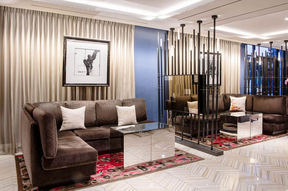 Luxury hotel lounge with brown velvet seating, cream curtains, framed artwork, and mirrored partition divider