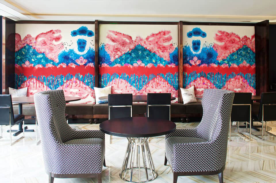 Modern lounge with colorful abstract art installation and patterned upholstered chairs around dark table