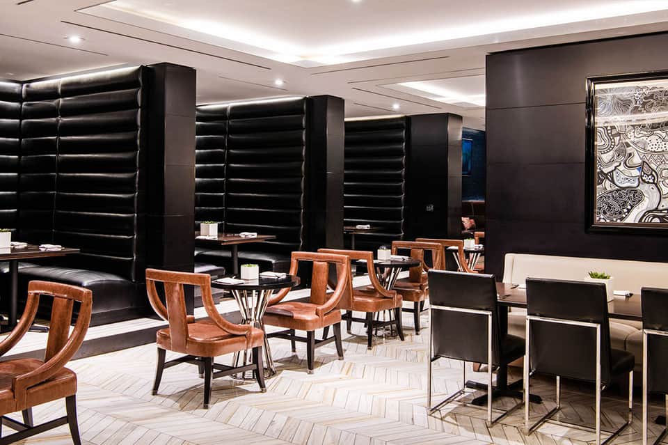 Modern hotel lounge with black padded walls, wooden chairs, and geometric floor pattern