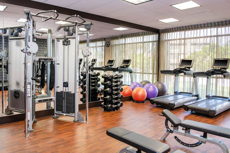Modern fitness center with exercise equipment, weight racks, treadmills, and exercise balls on wooden flooring
