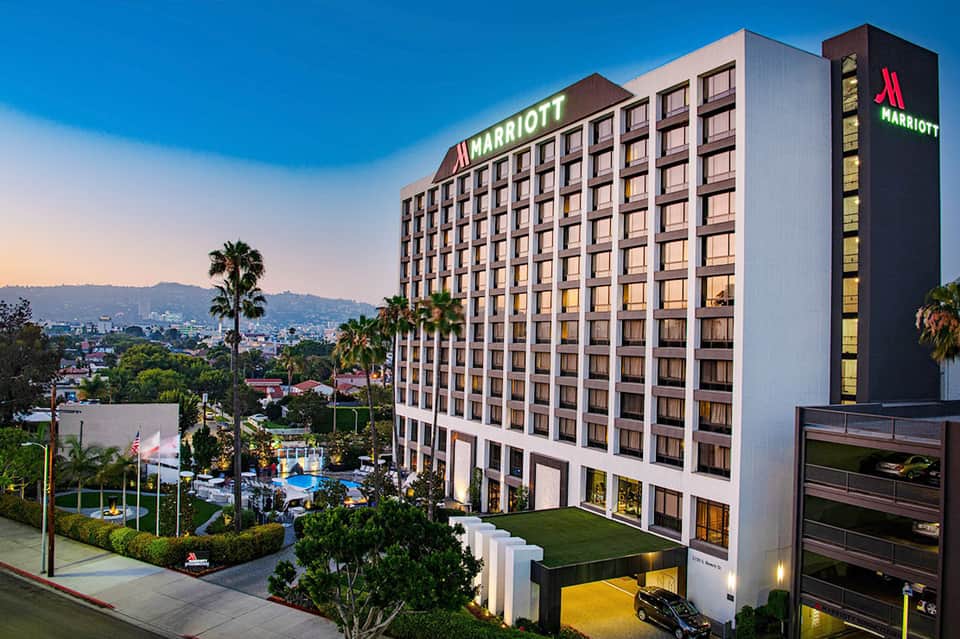 Modern Marriott hotel exterior with multi-story building, palm trees, and illuminated pool area at dusk