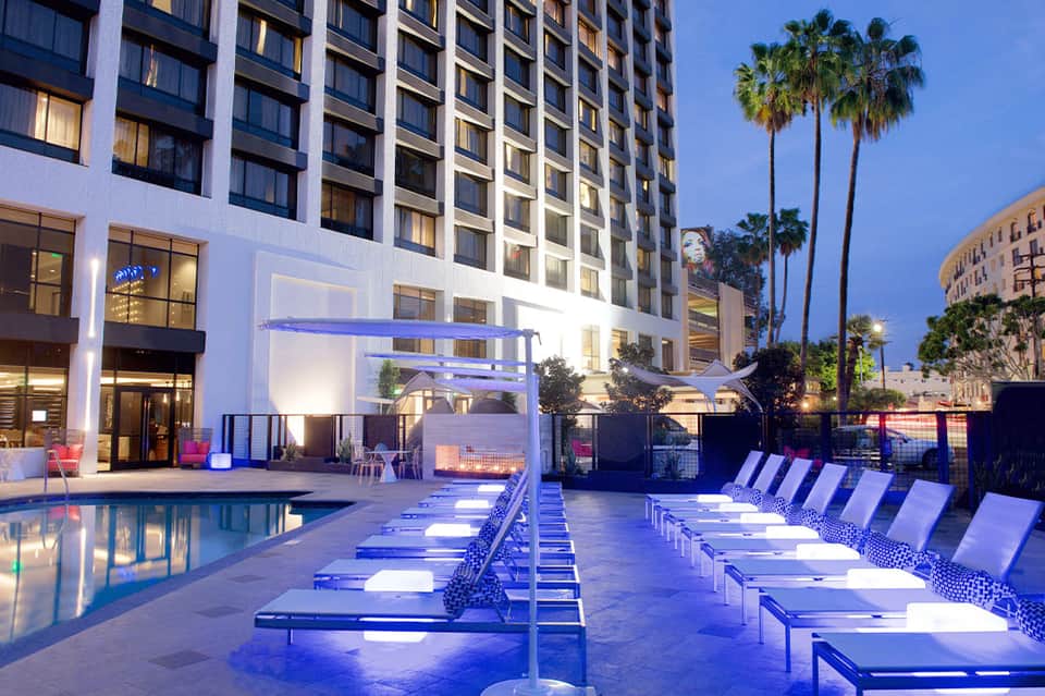 Modern hotel pool deck at dusk with blue lounge chairs and illuminated buildings