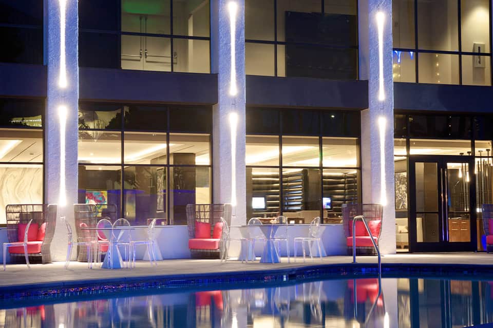 Contemporary poolside bar and lounge area at night with red chairs, blue lighting, and modern architecture