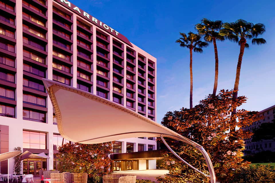 Marriott hotel exterior at dusk with pink lighting, curved architectural canopy, and tall palm trees