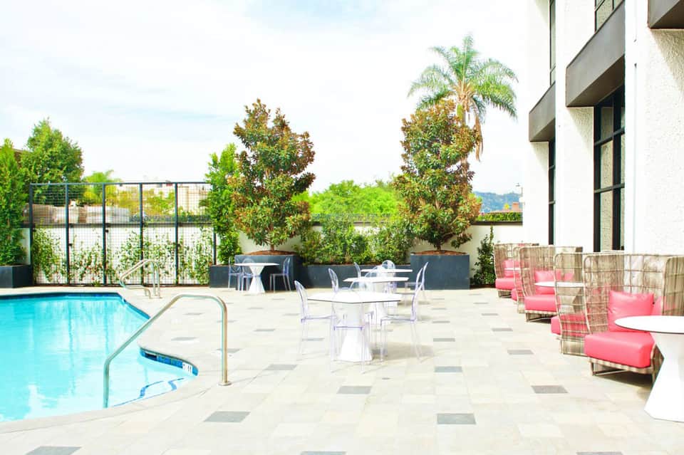Modern resort pool deck with lounge chairs, umbrellas, palm trees, and contemporary architecture