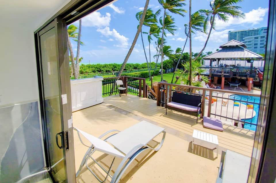 Beachfront balcony with lounge chairs overlooking pool, gazebo, and palm trees