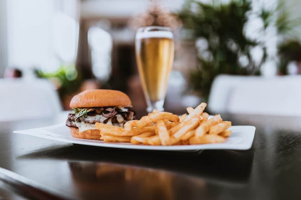Gourmet burger and fries served with champagne on white plate overlooking resort