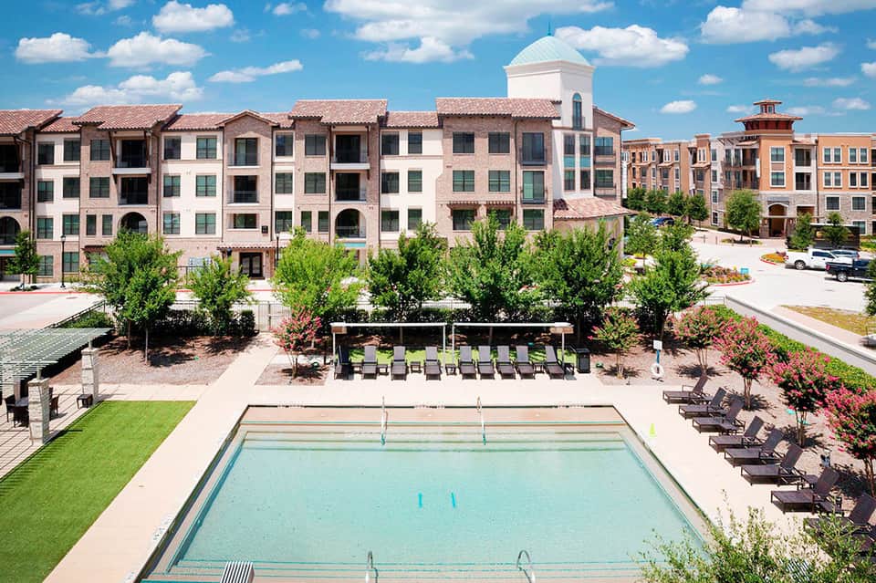 Resort courtyard with lap pool, Mediterranean-style building, manicured landscaping, and loungers
