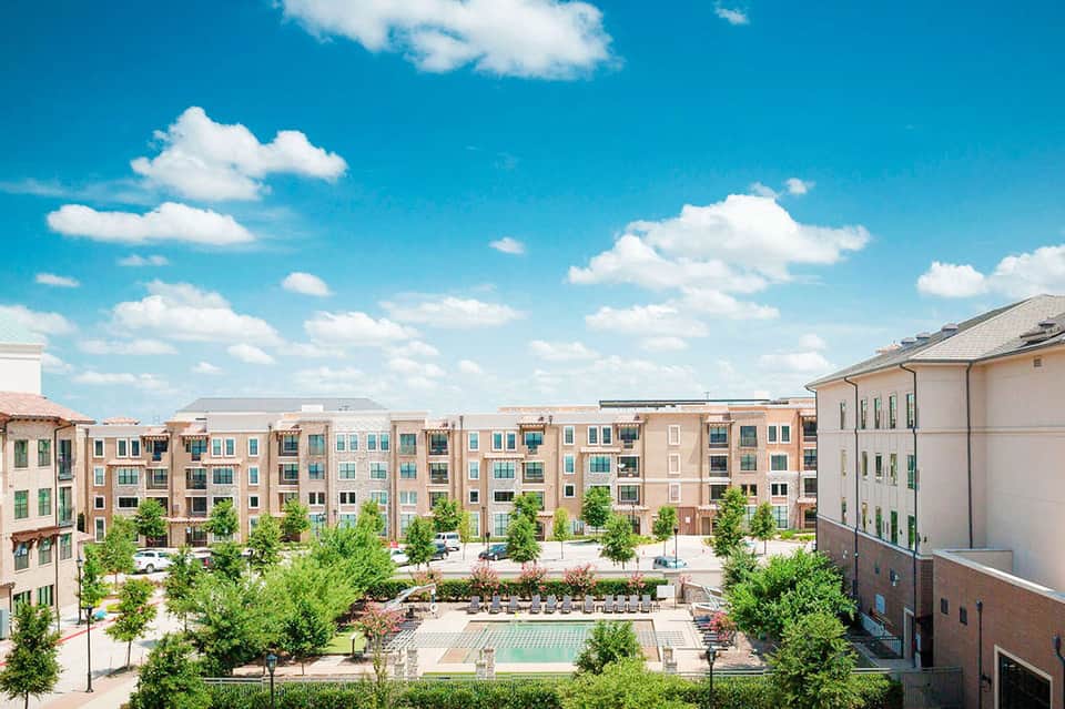 Urban residential complex courtyard with pool, surrounding buildings, trees, and clear blue sky