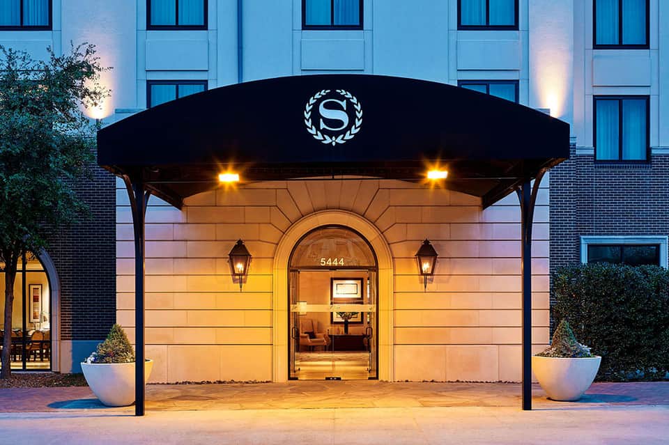 Elegant hotel entrance at dusk with black awning, illuminated doors, brick facade, potted plants, modern architecture