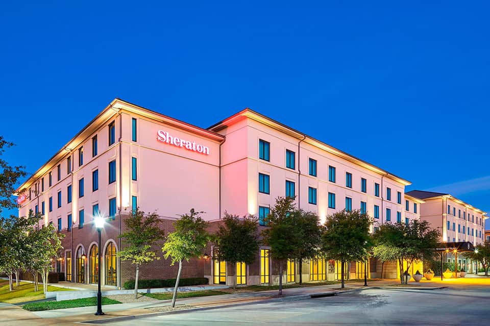 Pink Sheraton hotel exterior at dusk with illuminated windows and manicured grounds