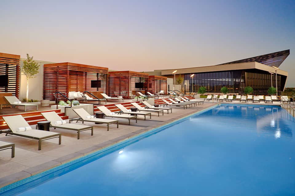 Resort pool deck with lounge chairs, wooden privacy screens, and modern building architecture