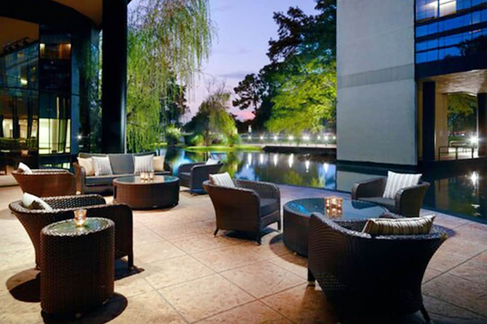 Modern outdoor patio with dark wicker seating, fire pits, and illuminated waterway at dusk