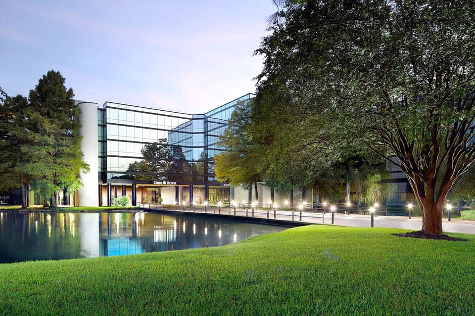Modern glass building reflected in calm pond with manicured lawn and trees