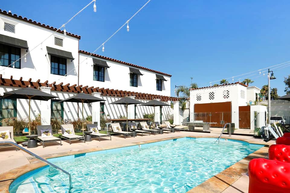 Contemporary pool area with white pergola, lounge chairs, and Spanish colonial-style building