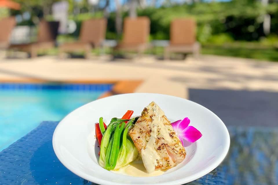 Grilled fish fillet with green vegetables and sauce served poolside on white plate