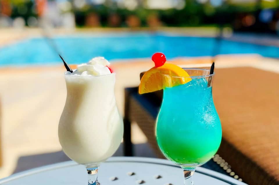 Two colorful cocktails by the pool with tropical garnishes and ocean backdrop