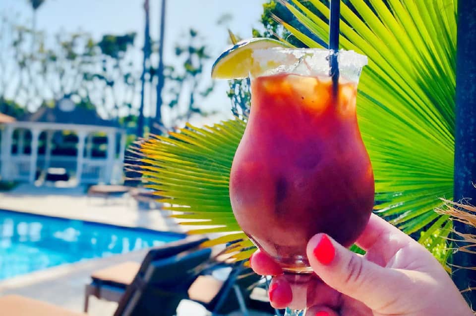 Colorful tropical drink with lime garnish held poolside with palm fronds and lounge chairs