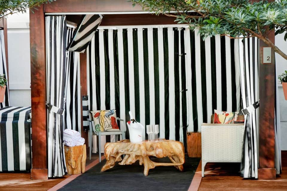 Luxury cabana with black and white striped curtains, wooden bench, and colorful pillows overlooking a terrace