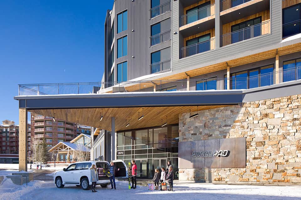 Modern resort entrance with stone facade, wooden accents, white SUV, and snow-covered ground