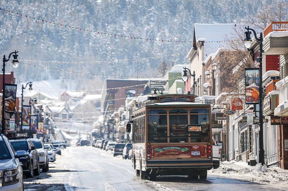 Historic cable car on snowy mountain town street with buildings and evergreen trees