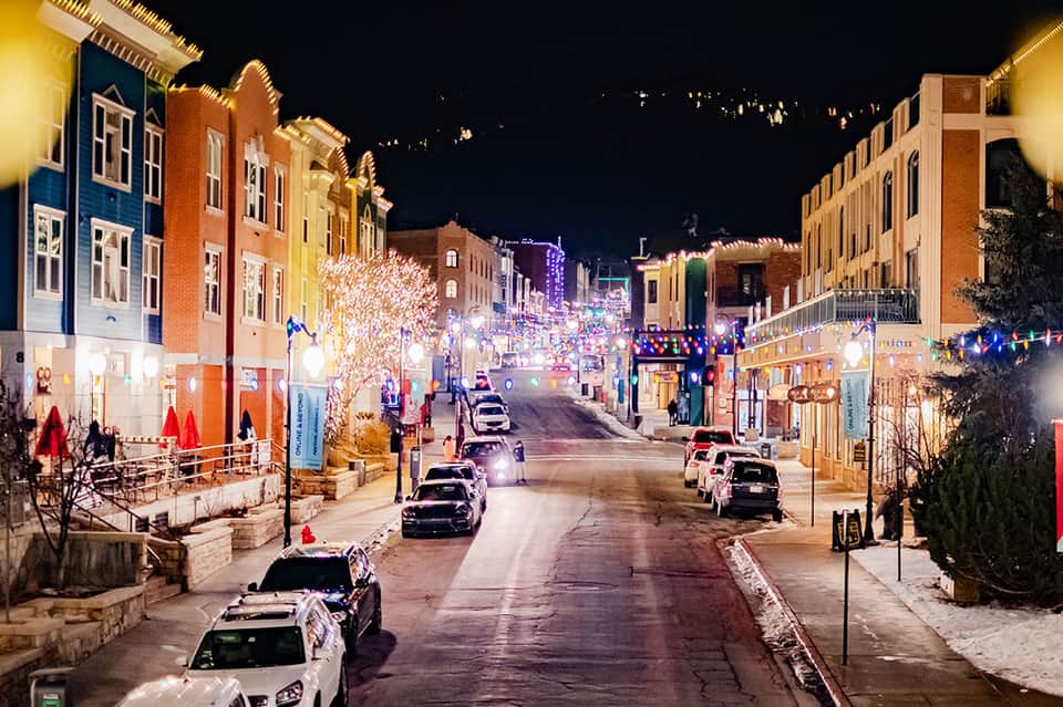 Holiday-decorated downtown street at night with brick buildings, festive lights, and parked cars