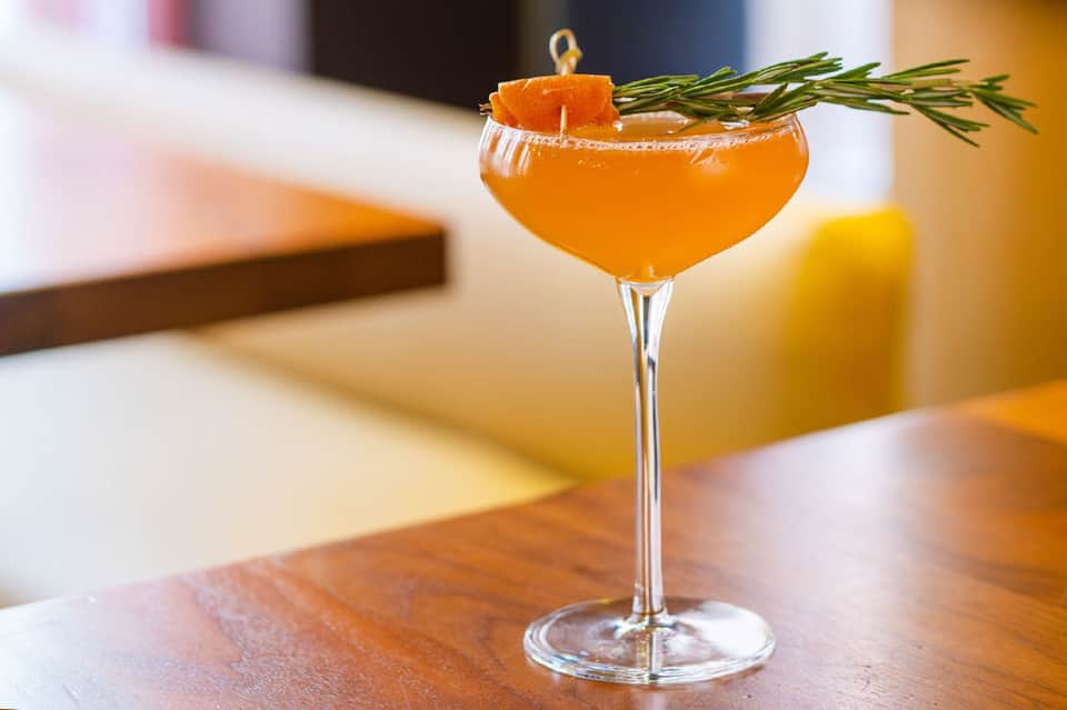 Orange cocktail with grapefruit slice and rosemary sprig in coupe glass on wooden table