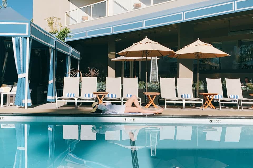 Woman relaxing poolside on lounge chair with umbrellas and cabanas reflected in clear water