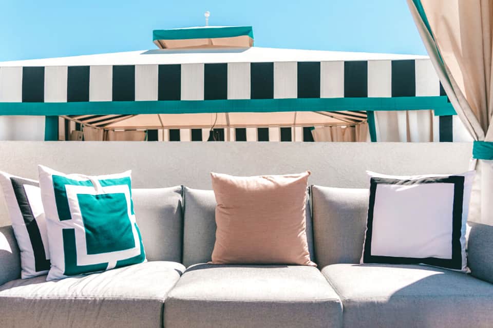 Beachside lounge sofa with teal and white striped awning and decorative pillows against blue sky