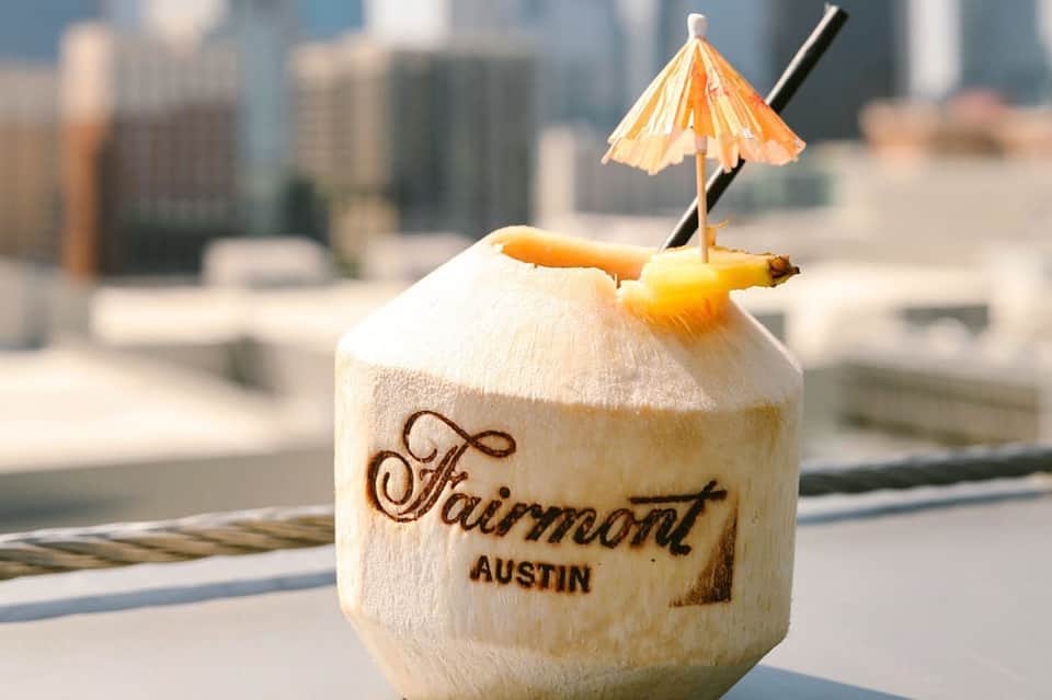 Coconut drink with decorative umbrella and straw on rooftop terrace with Fairmont Austin branding