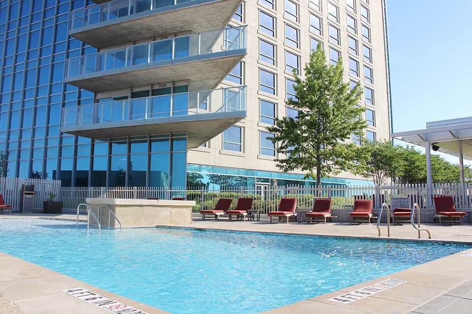 Modern high-rise hotel with outdoor swimming pool, red lounge chairs, and glass balconies overlooking water