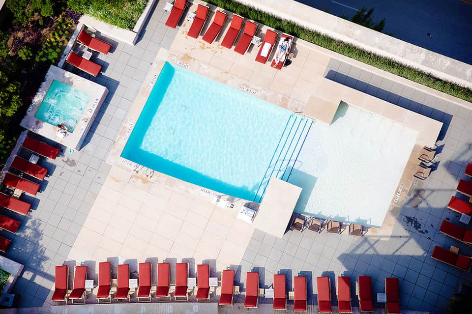 Aerial view of resort pool with turquoise water, red lounge chairs, and surrounding patio deck
