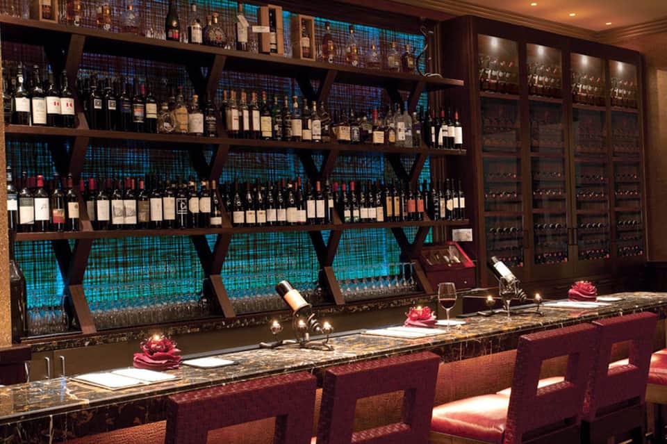 Upscale wine bar with extensive bottle collection on wooden shelves and teal backlighting