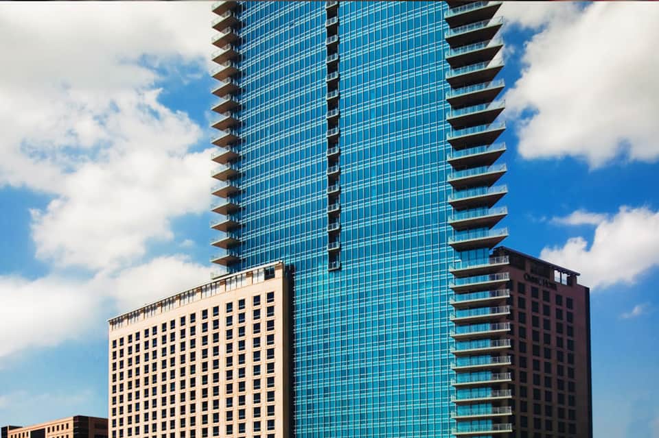 Tall modern glass high-rise hotel building next to historic cream-colored building against blue sky