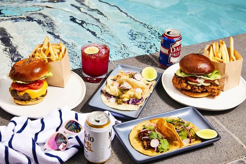 Poolside lunch spread with burgers, tacos, fries, and beverages by the water